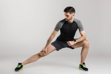 Spor giyimli genç bir sporcunun gri arka planda tek başına egzersiz yaparken görüntüsü