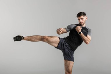 Gri arka plan üzerinde izole edilmiş yakışıklı, güçlü bir sporcu görüntüsü boks egzersizleri yaptırıyor..
