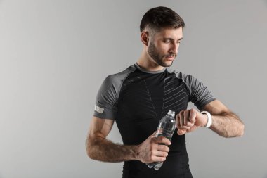 Gri arka planda izole edilmiş akıllı kaset kullanırken spor giyim sektöründe su içen genç ve güçlü bir adamın görüntüsü