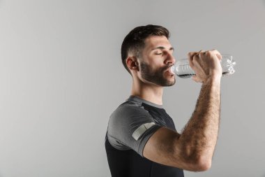 Gri arka planda izole bir şekilde çalışırken spor giyim ve içme suyu içinde genç ve güçlü bir adamın görüntüsü.