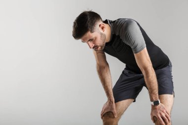 Gri arka planda izole bir şekilde çalışırken spor giysileri içinde dinlenen genç bir adamın görüntüsü