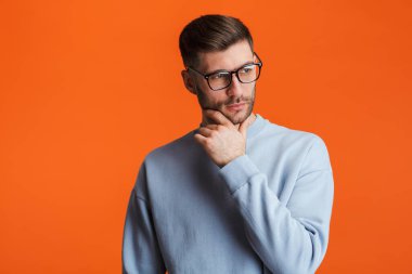 Gözlüklü genç sakallı yakışıklı bir adam portakal rengi arka planda izole edilmiş kameraya poz veriyor.