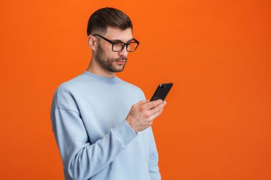 Gözlük takan sakallı yakışıklı bir adamın portakal rengi arka planda izole edilmiş cep telefonu görüntüsü.