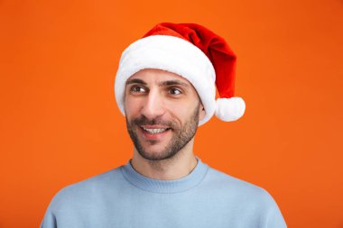 Noel Baba şapkalı iyimser bir gencin portakal rengi duvar arkasına izole edilmiş pozu..