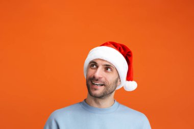 Noel Baba şapkalı iyimser bir gencin portakal rengi duvar arkasına izole edilmiş pozu..