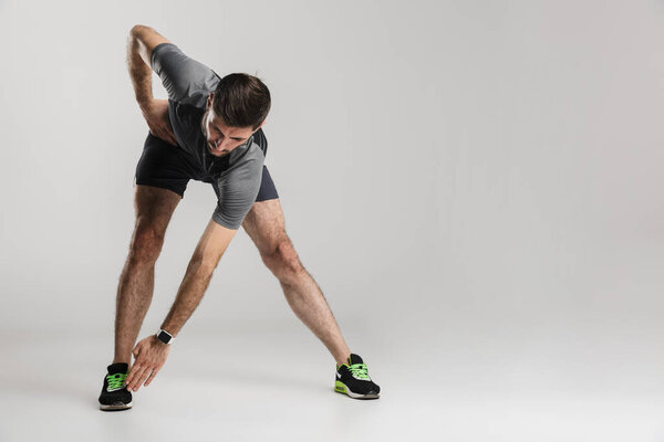Image of caucasian athletic man in sportswear doing exercise while working out isolated over gray background