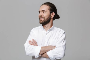 Genç, iyimser, yakışıklı ve sakallı bir adamın gri duvar arkasında yalnız poz vermesi..