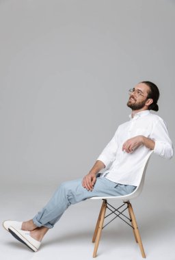 Genç, mutlu, iyimser, yakışıklı, sakallı bir adamın, gri duvar arkasında gözlük takarak poz verişi..