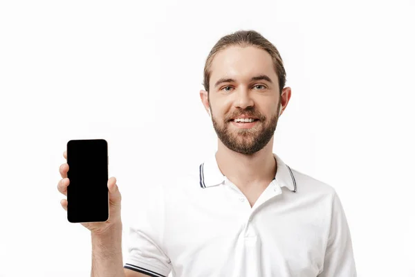 照片中 一个年轻快乐英俊的大胡子男子在白色墙壁的背景下 用手机聆听音乐 耳机显示他的表演 — 图库照片