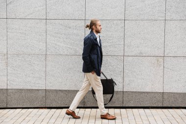 Çekici, kendine güvenen, genç, sakallı bir iş adamı sokakta elinde evrak çantasıyla dolaşıyor.