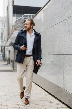 Çekici, kendine güvenen genç, sakallı iş adamı sokakta yürüyor, evrak çantası taşıyor, cep telefonu kullanıyor.