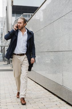 Çekici, kendine güvenen genç, sakallı iş adamı sokakta yürüyor, evrak çantası taşıyor, cep telefonuyla konuşuyor.