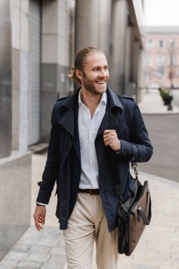 Çekici, mutlu, sakallı bir iş adamı sokakta elinde evrak çantasıyla dolaşıyor.