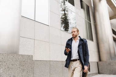 Çekici, kendine güvenen genç, sakallı iş adamı sokakta yürüyor, evrak çantası taşıyor, cep telefonu kullanıyor.