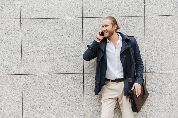 Handsome happy young bearded businessman standing outdoors in the street