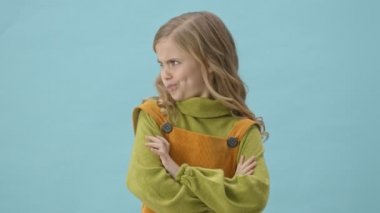 Genç hoşnutsuz kız her iki tarafa da bakıyor ve mavi arka planda izole edilmiş baş parmak hareketi gösteriyor.