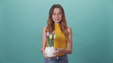 Neşeli genç kız Paskalya yumurtalarını kutluyor ve onları mavi arka planda izole edilmiş kameraya gösteriyor.