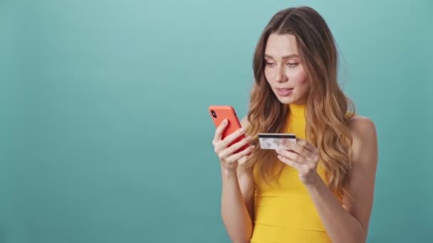 유쾌하게 매력적 소녀가 인터넷 쇼핑을 고립된 배경에서 신용카드와 스마트폰을 사용하여 — 비디오