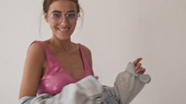 Gülümseyen şık, güzel esmer kadın mayo ve gözlüklü dans eden ve gri arka planda kameraya bakan.