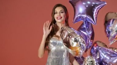 Parlak pullu, neşeli bir kadın. Kırmızı arka planda balonlarla eğleniyor.