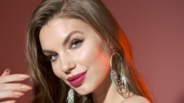 Şehvetli, gizemli, parlak pullu elbisesi olan, saçlarına dokunan ve kırmızı arka plandaki kameraya bakan kadının yakın görüntüsü.