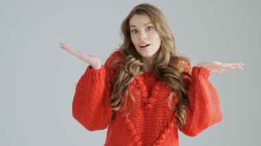 Neşeli genç bir kadın sürpriz bir şekilde elini kaldırıyor. Stüdyodaki gri bir arka plandan izole edilmiş.