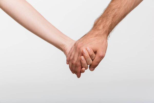 Closeup photo of a man and woman holding hands of each other isolated over white wall background.