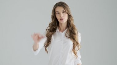 Ofis kıyafetleri içindeki güzel genç bir kadın stüdyodaki gri arka planda izole edilmiş hoş bir jest yapıyor.