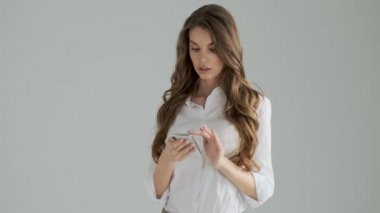 Güzel bir kadın, atölyedeki gri arka plandan izole edilmiş akıllı telefonunu kullanarak birine el sallıyor.