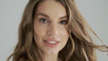 Cilveli, baştan çıkarıcı bir kadının yakın plan görüntüsü stüdyodaki gri bir arka plan üzerinden kameraya hava öpücüğü gönderiyor.