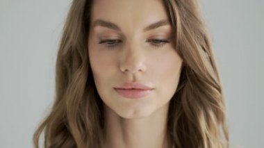 Sakin bir kadının yakın plan görüntüsü, gözlerini stüdyodaki gri bir arkaplanda izole edilmiş kameraya açıyor.