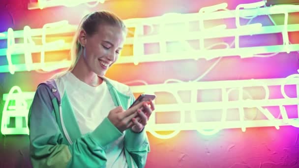 Skrattande Ung Kvinna Använder Smartphone Över Flerfärgad Neon Text — Stockvideo