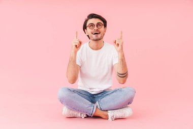 Gözlük takan mutlu bir adamın, pembe arka plan üzerinde bacak bacak bacak üstüne atarak oturduğu bir sahne.