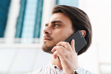 Çizgili tişört giyen, cep telefonuyla konuşan ve şehir caddesinde yürürken yan bakan genç adamın fotoğrafı.
