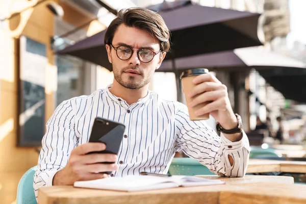 Photo Focused Unshaven Man Wearing Eyeglasses Typing Cellphone Drinking Coffee — Stock Photo, Image