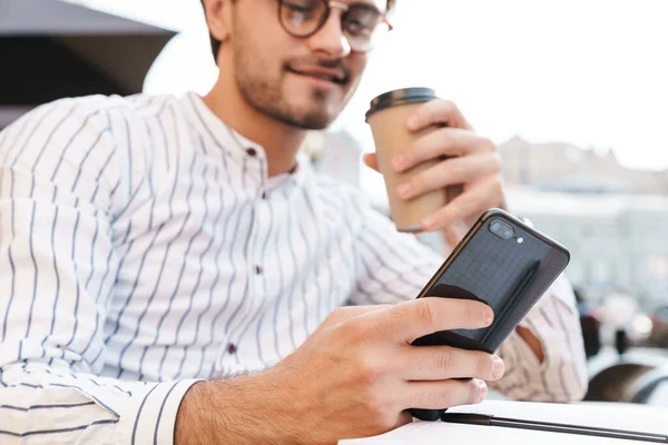 照片中快乐的成功人士在户外咖啡店工作时 戴着眼镜 喝咖啡 在手机上打字 — 图库照片