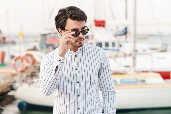 Photo Successful Masculine Man Wearing Sunglasses Standing Looking Aside While — Stock Photo, Image