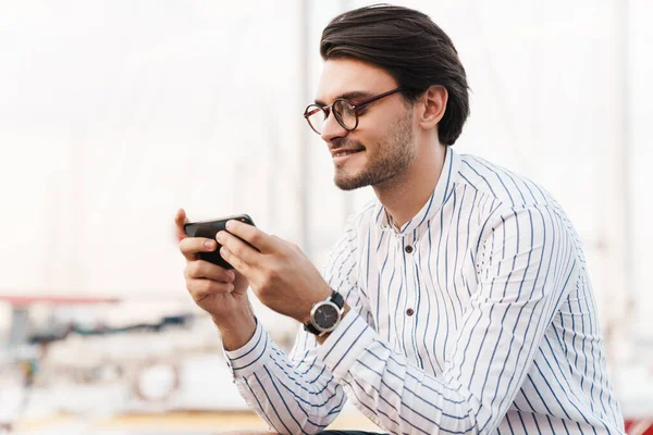 Photo Handsome Unshaven Man Wearing Eyeglasses Typing Cellphone Smiling While — Stock Photo, Image