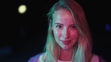 Kafkasyalı güzel bir kadının yakın çekim görüntüsü gece parlak neon ışıklarının üzerinden kameraya bakıyor.