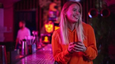 Mutlu, genç, sarışın bir kadın gece kulübünde vakit geçirirken telefonunu kullanıyor.