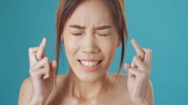 Asyalı hoş bir kadın parmaklarını çapraz tutarken mavi duvar arkasında izole edilmiş bir dilek tutuyor.