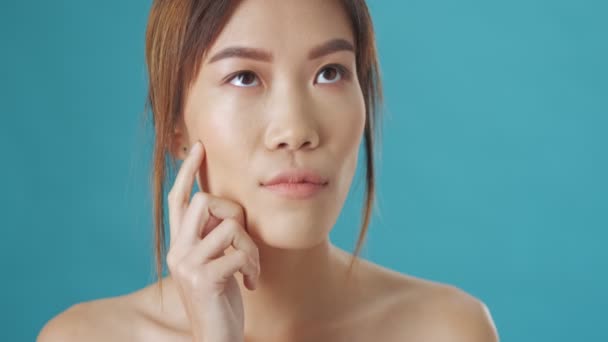 深刻なアジア系女性が青い壁の背景に孤立した何かを考えている — ストック動画