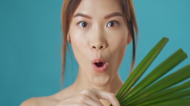 一位情绪激动的年轻亚洲女人 在蓝色的墙壁背景上 把一片绿叶从一边移到另一边时 表现出不同的情绪 — 图库视频影像