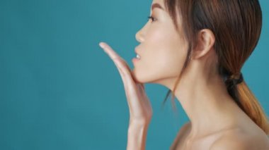 Gülümseyen Asyalı genç bir kadının yan görüntüsü mavi duvarın üzerinden hava öpücüğü gönderiyor.