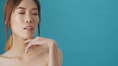 Güzel, çekici, genç Asyalı bir kadın avucunun içinde mavi duvar arka planında bir kopya alanı gösteriyor.