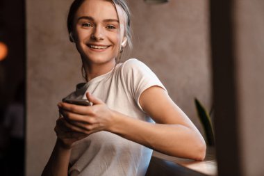 Güzel bir kadının rahat bir kafede otururken kulaklık ve cep telefonu kullandığı fotoğraf.