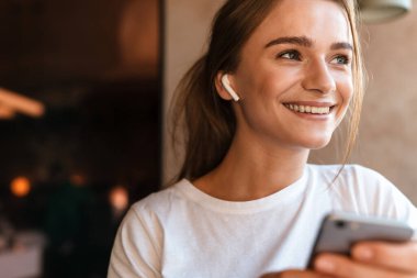 Güzel bir kadının rahat bir kafede otururken kulaklık ve cep telefonu kullanması.