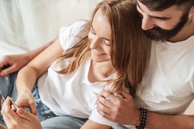 Mutlu genç bir çiftin gülümseyen ve cep telefonunu kullanırken görüntüsü.