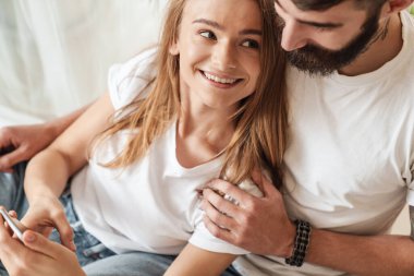 Mutlu genç bir çiftin gülümseyen ve cep telefonunu kullanırken görüntüsü.