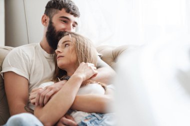 Romantik mutlu çiftin evde, aydınlık bir odada yatakta yatarken sarıldığı görüntüsü.